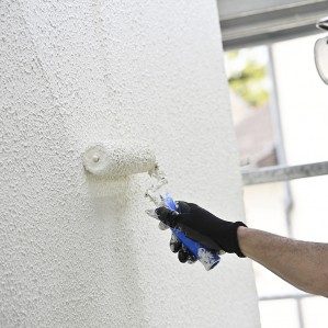 Peinture de façade à Salon-de-Provence Un homme peint un mur blanc avec un rouleau, portant des gants et des lunettes de protection.